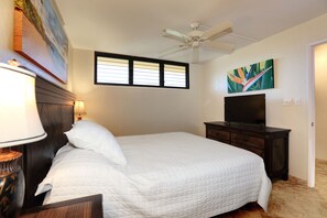 A bedroom with a bed, a ceiling fan, a television on a dresser, a window with blinds, and a painting on the wall. - Kihei Surfside, #511 1 Bedroom Condo by RedAwning (Kihei)