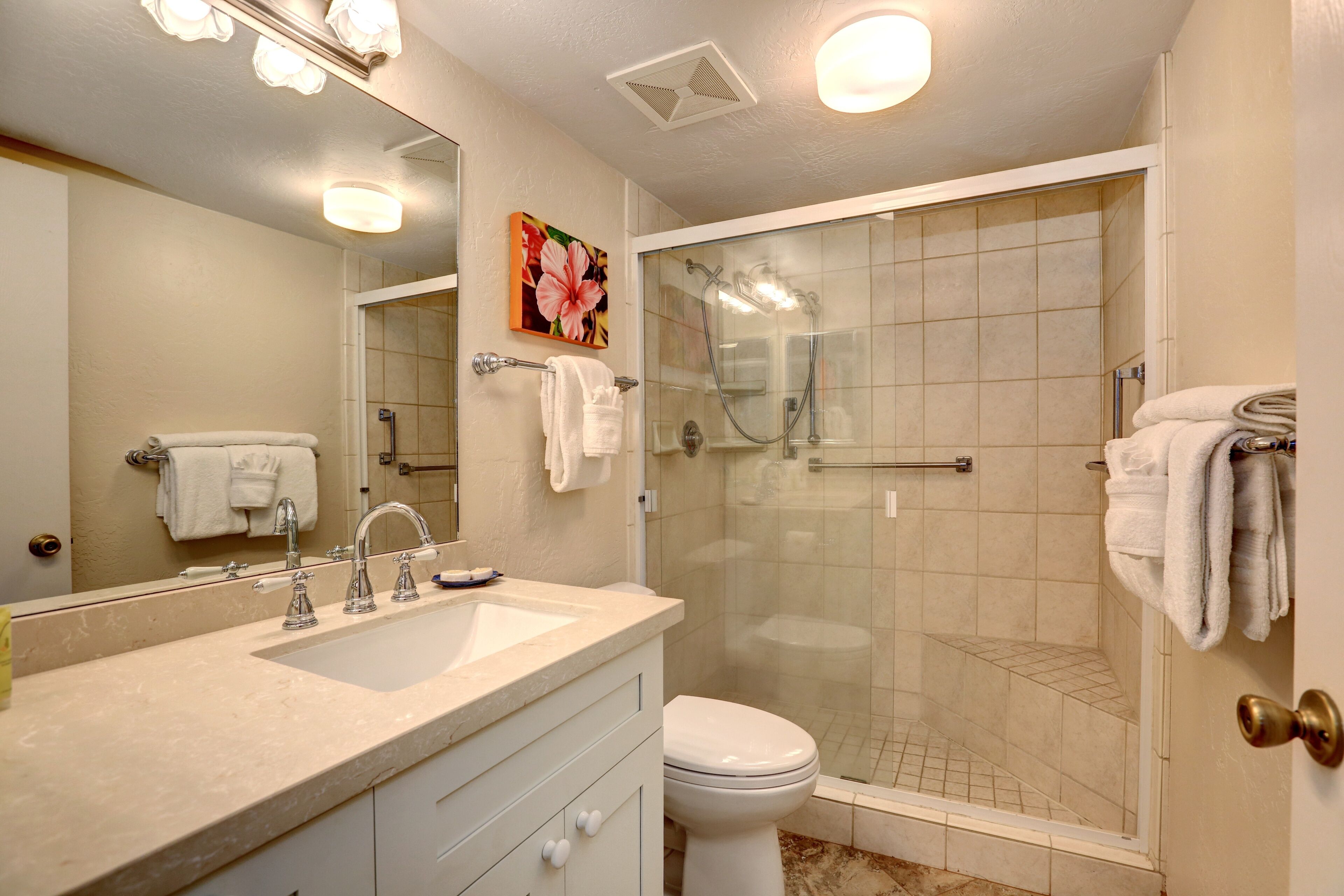 A bathroom with a glass-enclosed shower, a sink with a mirror, and a toilet.