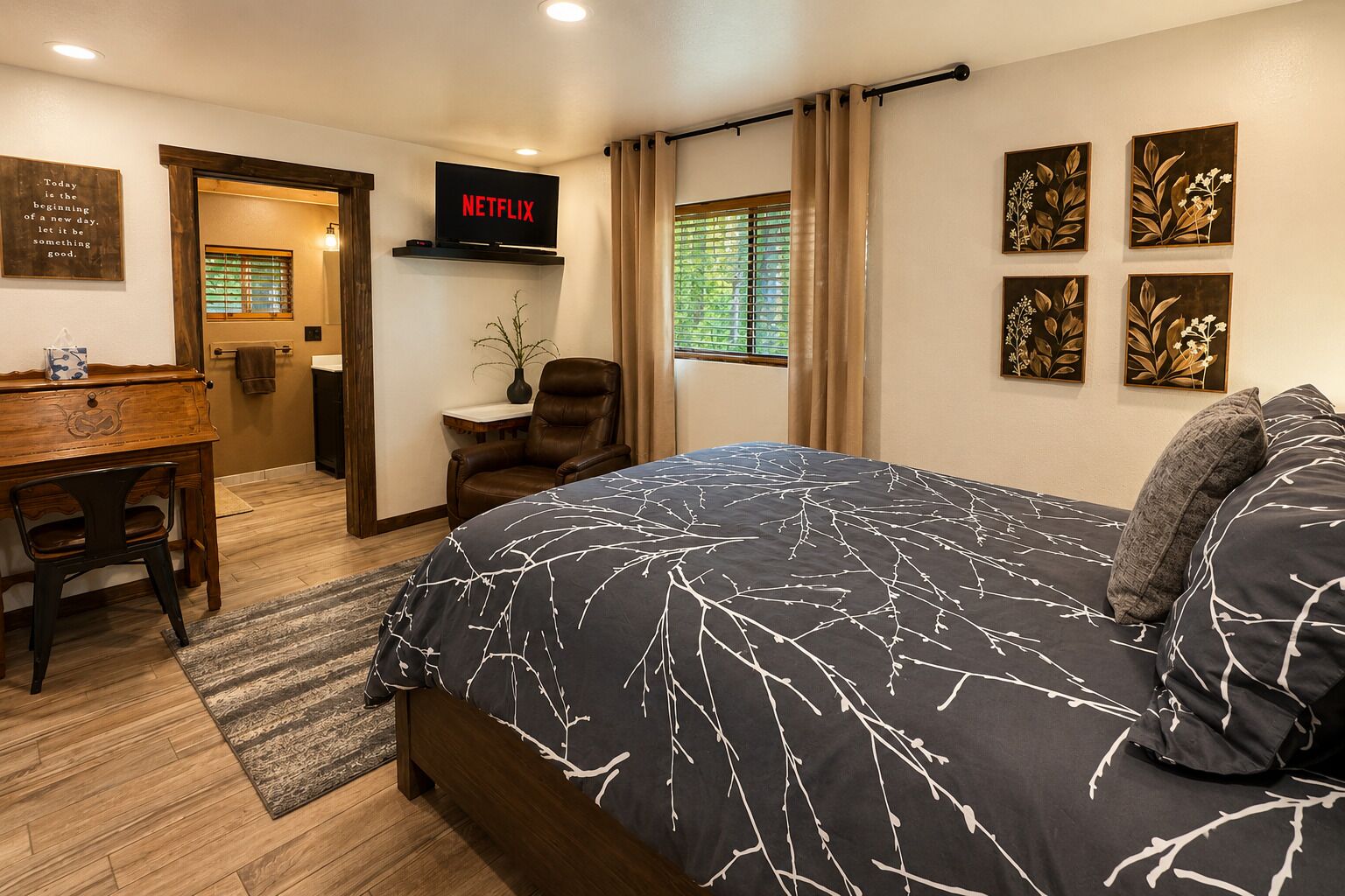 A bedroom with a bed, a desk, a chair, a TV, and artwork on the walls.