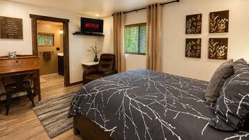 A bedroom with a bed, a desk, a chair, a TV, and artwork on the walls.