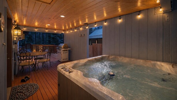 A wooden deck with a hot tub, outdoor seating, and string lights. - Alpine Getaway 2 Bedroom Home by RedAwning (Leavenworth)