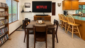 Un coin repas équipé d’un téléviseur diffusant du contenu « NETFLIX », d’une cheminée, de chaises en bois et d’une bibliothèque remplie de DVD.