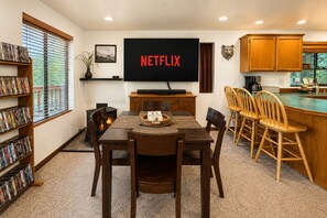 Un coin repas équipé d’un téléviseur diffusant du contenu « NETFLIX », d’une cheminée, de chaises en bois et d’une bibliothèque remplie de DVD.
