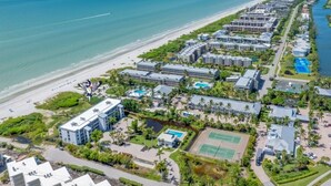 An aerial view of a coastal hotel with multiple buildings, a beach, and a tennis court. - Pelicans Roost 203 2 Bedroom Condo by RedAwning (Sanibel)