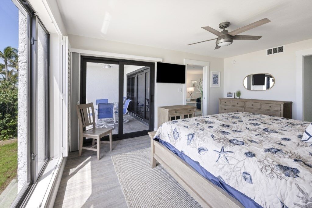 Ein Schlafzimmer mit einem Bett, einem Sessel, einem Schreibtisch, einem Deckenventilator und einer Glastür zu einem Balkon.