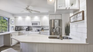 A modern kitchen with white cabinetry, a stainless steel refrigerator, a built-in island with a sink, and a ceiling fan. - Loggerhead 282 2 Bedroom Condo by RedAwning (Sanibel)