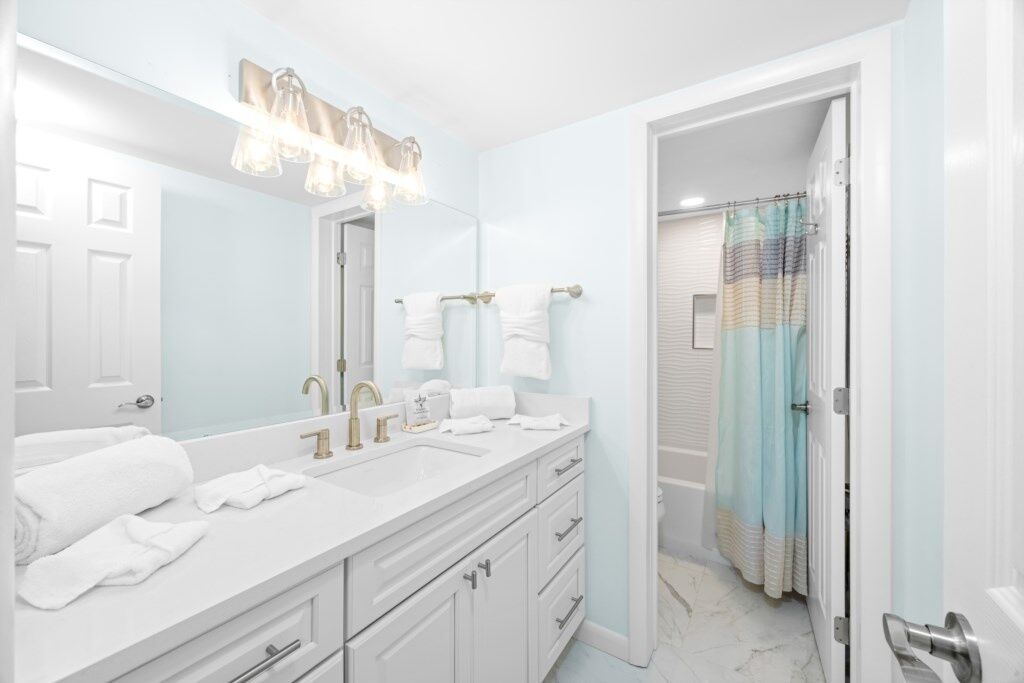 A bathroom with a white vanity, two sinks, a large mirror, and a shower curtain.