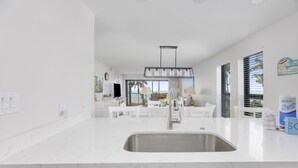 Una cocina moderna con encimera blanca, pileta de acero inoxidable y una zona de comedor con mobiliario blanco.