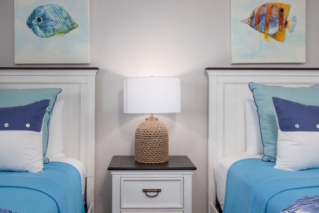 Une chambre avec deux lits, chacun recouvert d’une couverture bleue assortie à des coussins. Une petite table de chevet avec une lampe et un objet décoratif se trouve entre les deux lits.