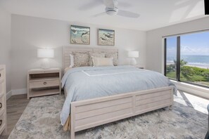 A bedroom with a bed, nightstands, and a view of the ocean. - Pelicans Roost 303 2 Bedroom Condo by RedAwning (Sanibel)