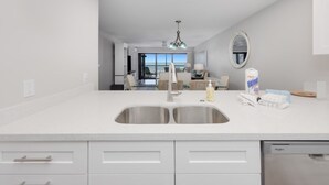 Una cocina moderna con un lavamanos doble, armarios blancos y vistas al comedor.