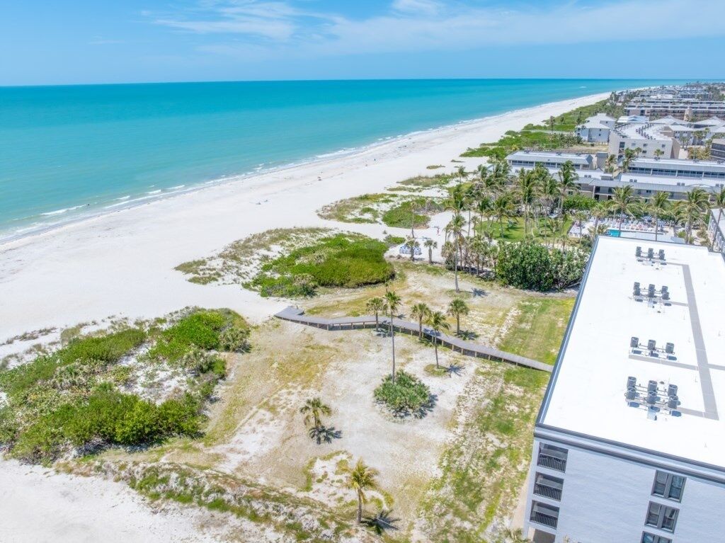 An aerial view of a beachfront property with a white building, a sandy beach, and palm trees.