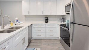 Una cocina moderna con gabinetes blancos, electrodomésticos de acero inoxidable y una cafetera sobre la encimera.