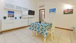 Un comedor con una mesa dispuesta para dos personas, armarios blancos, un televisor montado y obras de arte en las paredes.