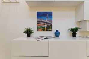 Un comptoir d’accueil orné d’un tableau représentant un pont, de plantes en pot et d’un vase bleu.