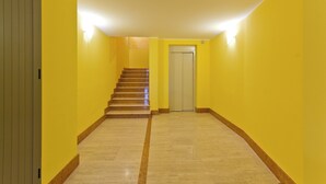 Un pasillo con paredes amarillas, suelo de mármol y una escalera que lleva a una puerta.