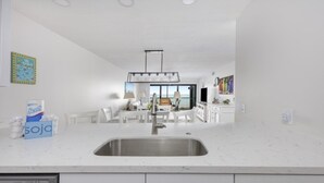 Una cocina moderna con armarios blancos, una isla grande con un fregadero y un comedor con sillas blancas.