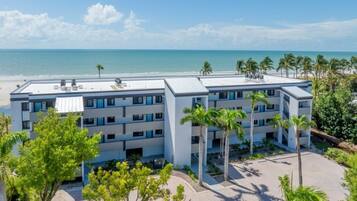 Un hotel de varios pisos con piscina en la azotea, rodeado de palmeras y vistas a la playa.