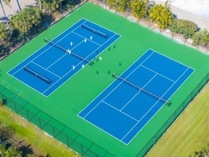 En vy från ovan av ett tennisanläggning med två banor, omgiven av ett staket och belägen intill en strand.