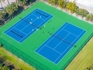 An aerial view of a tennis court complex with two courts, surrounded by a fence and palm trees.