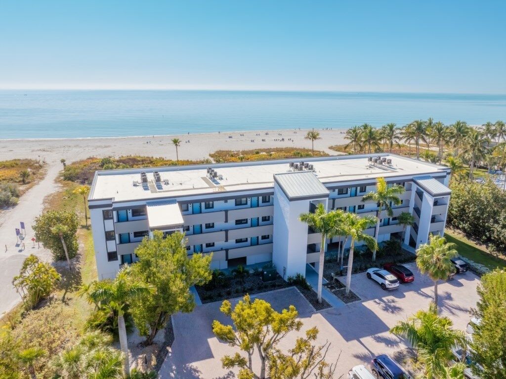 Un hôtel à plusieurs étages, doté d’un toit plat, situé près d’une plage bordée de palmiers.