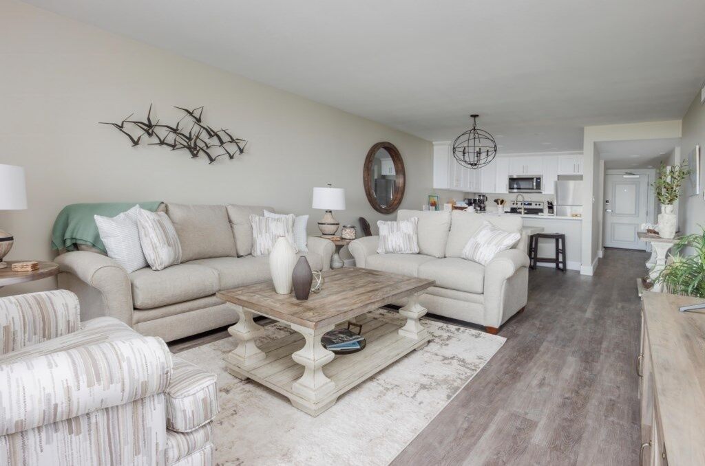 A living room with a beige sofa, a coffee table, and a patterned ottoman.