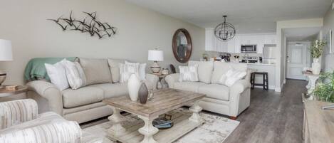 A living room with a beige sofa, a coffee table, and a patterned ottoman.