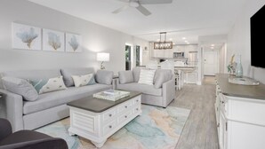 A modern living room with a grey sofa, a coffee table, and a chandelier. - Pelicans Roost 101 2 Bedroom Condo by RedAwning (Sanibel)