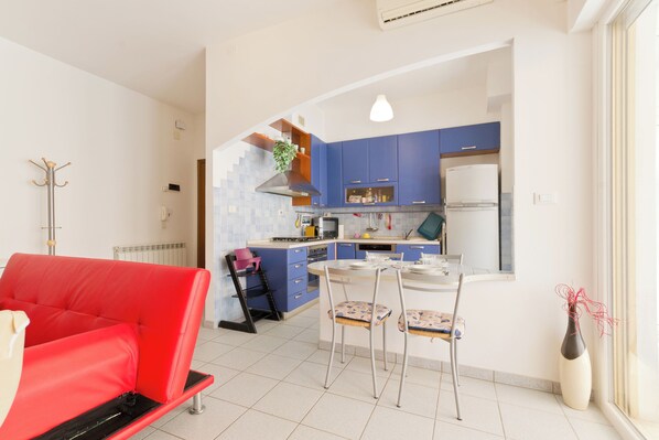 A modern kitchen with blue cabinets, a dining area with a red sofa, and a small island with chairs.