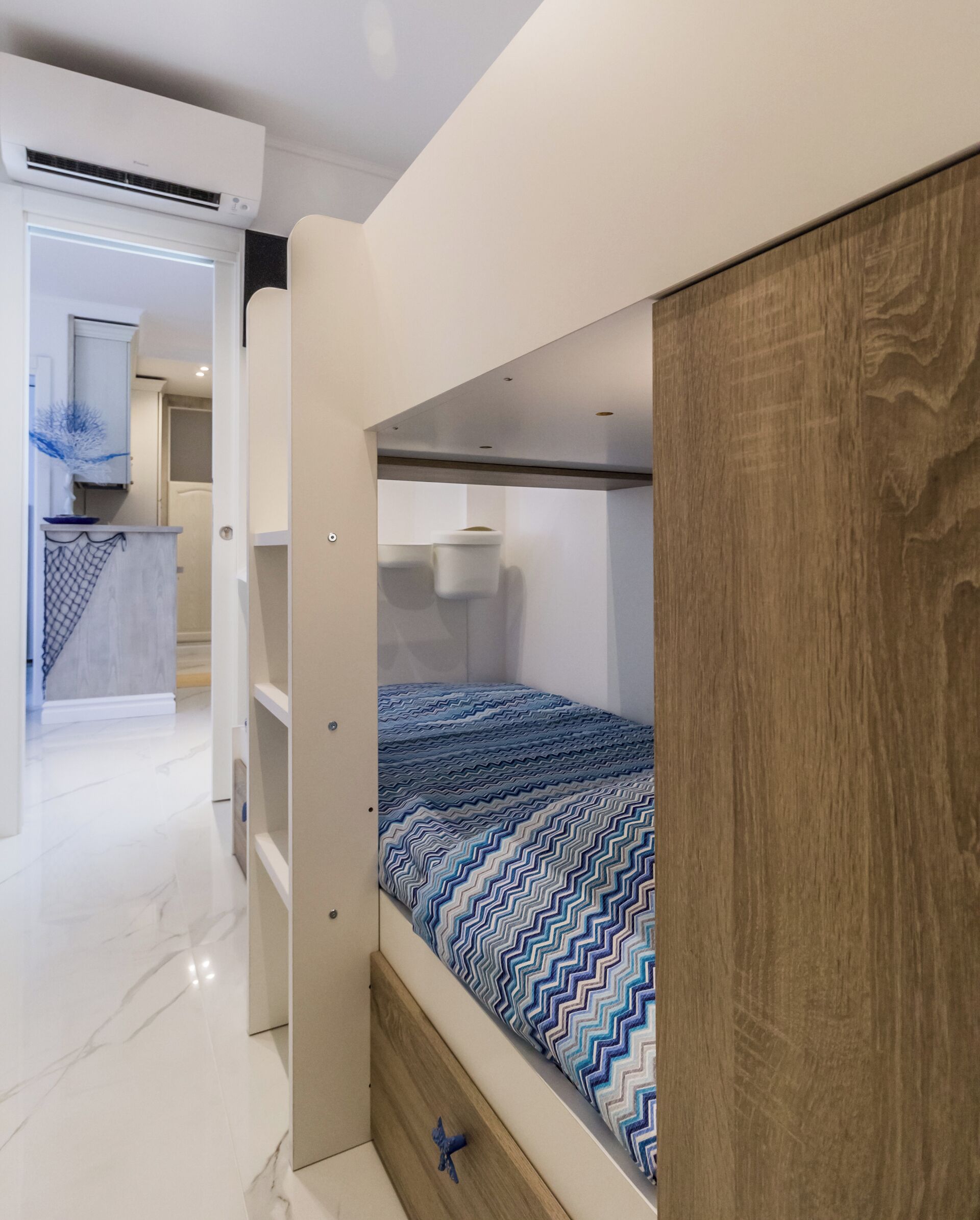 Een compacte slaapkamer met een stapelbed, een houten garderobe en een kleine badkamer.