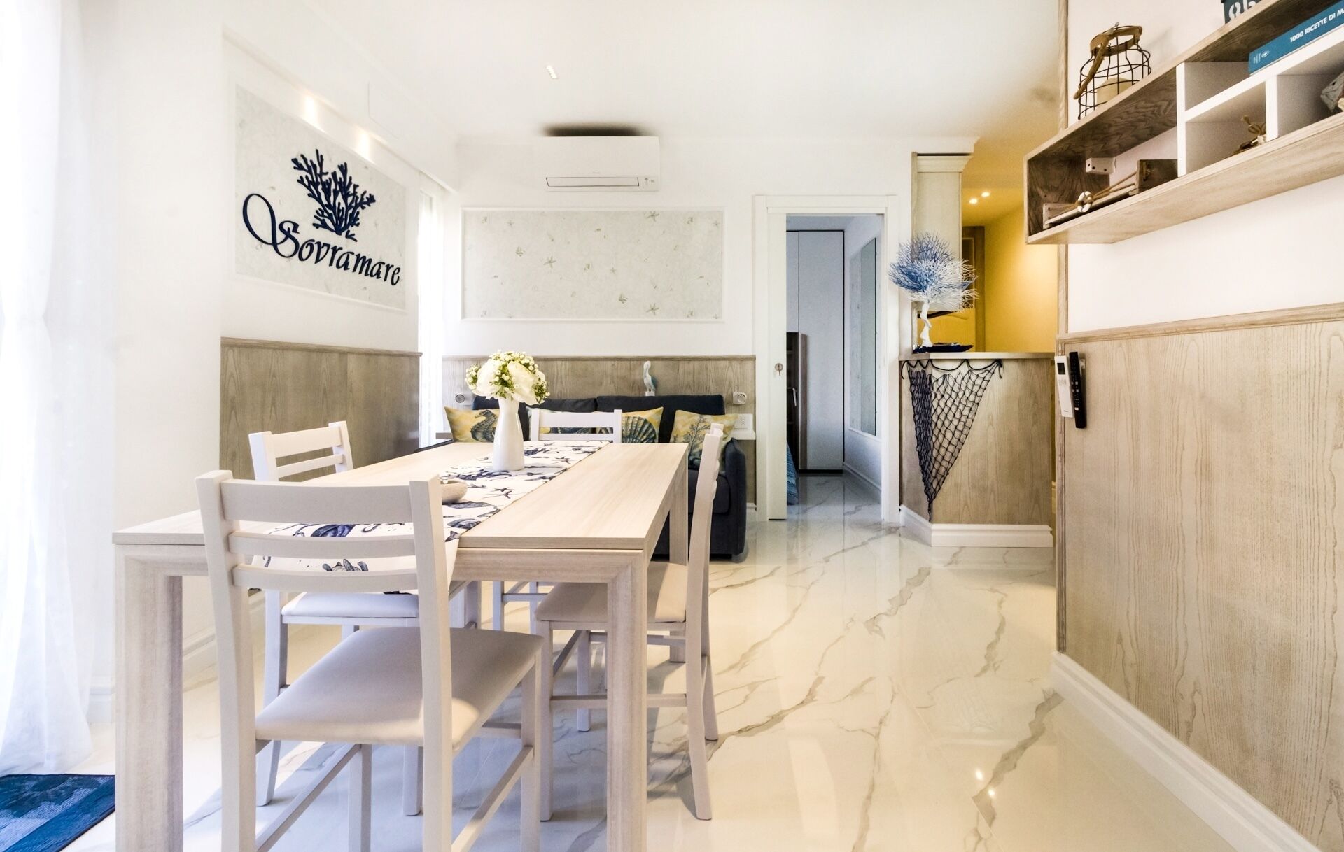 A modern kitchen with white cabinetry, a marble countertop, and a dining area with a white table and chairs.