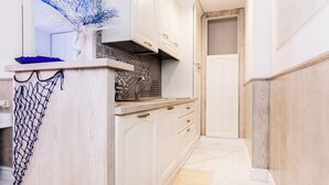 Une cuisine étroite avec des meubles blancs, un plan de travail en marbre et un vase bleu décoratif.