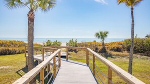 A wooden boardwalk leading to a beach with palm trees and a clear sky. - Pelicans Roost 207 2 Bedroom Condo by RedAwning (Sanibel)