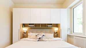 Un dormitorio con cama, almacenamiento integrado, lámparas de noche y una ventana.