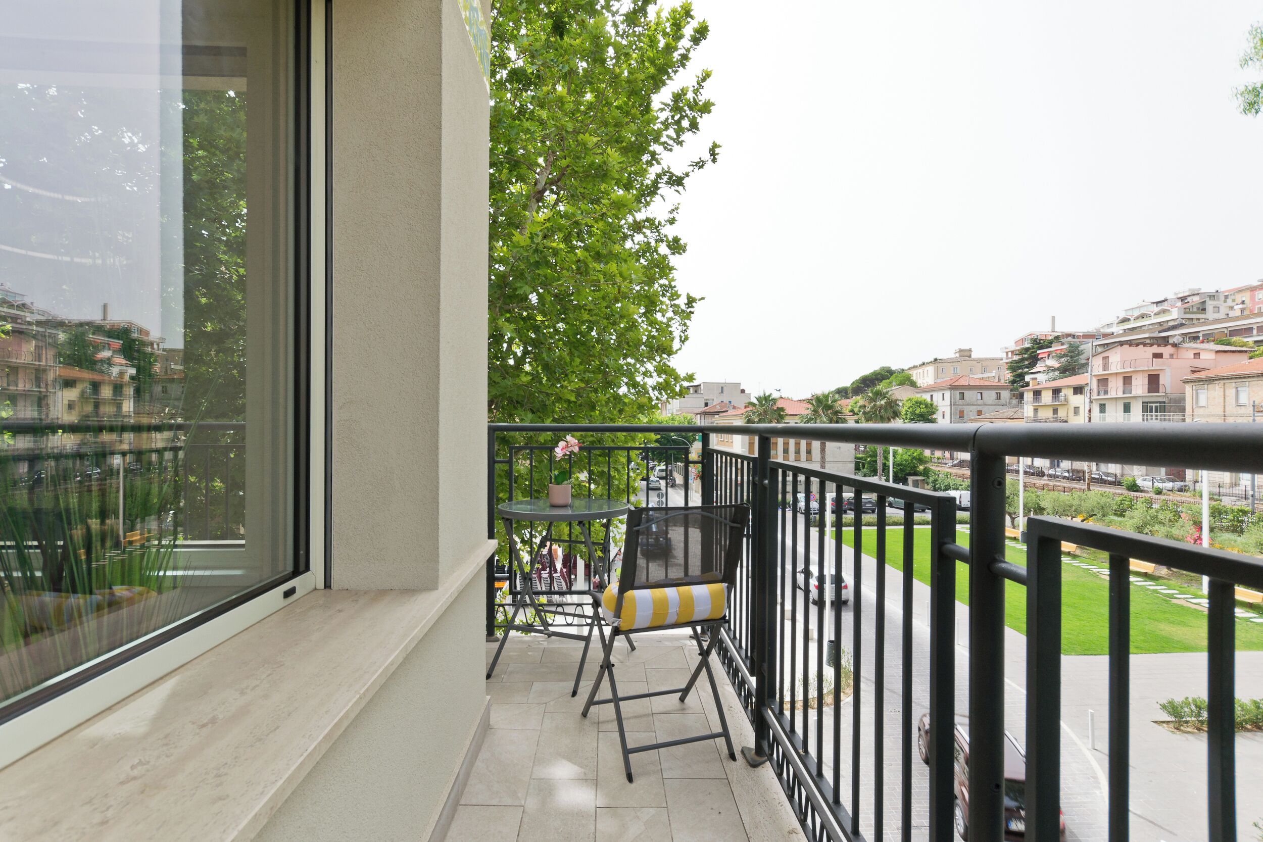 A balcony with a table and chairs, a view of a cityscape, and a railing.