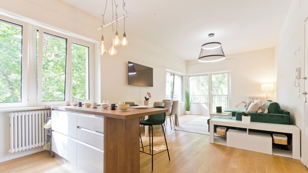 Una cocina moderna con una isla central, taburetes de bar y un área de comedor con sofá y televisor.