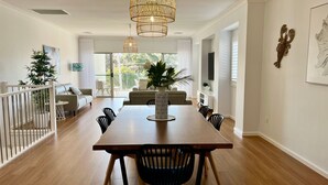 A dining area with a wooden table, black chairs, and a vase with plants. There is a staircase leading to a balcony with a view of trees. - Jo Sea by Book Jervis Bay - Luxury in Vincentia with Ocean Views (Vincentia)