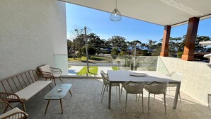 A balcony with a table and chairs, a sofa, and a view of a residential area. - Jo Sea by Book Jervis Bay - Luxury in Vincentia with Ocean Views (Vincentia)