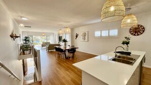 A spacious kitchen with a central island, pendant lights, and a dining area with a sofa and chairs. - Jo Sea by Book Jervis Bay - Luxury in Vincentia with Ocean Views (Vincentia)