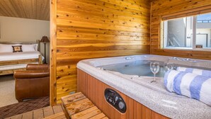 A wooden cabin interior with a hot tub, a bed, and a window.