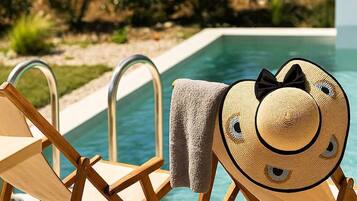 Zona junto a la piscina con sillones de madera y un sombrero de paja.