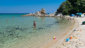 Une plage à l’eau claire, avec des formations rocheuses, où l’on peut voir des gens nager et prendre des bains de soleil.