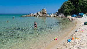 Una spiaggia con acque cristalline, formazioni rocciose e persone che nuotano e prendono il sole.