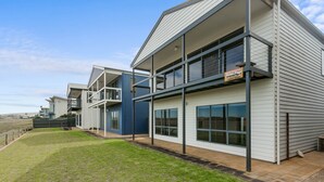 Un immeuble résidentiel moderne à plusieurs étages, doté de balcons, de grandes fenêtres et d’une pelouse bien entretenue.