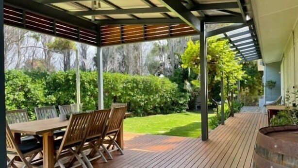 Une terrasse extérieure couverte, avec une table et des chaises en bois, entourée d’un jardin luxuriant et offrant une vue sur les arbres.