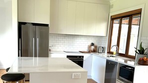 Une cuisine moderne avec des armoires blanches, un réfrigérateur en acier inoxydable, un four à micro-ondes encastré et un îlot central en bois doté de tabourets de bar.