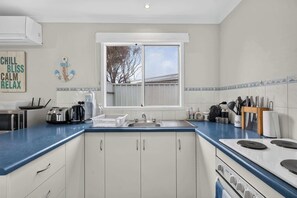 A kitchen with a window, white cabinets, a blue countertop, and various appliances.