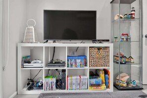 A living room with a flat-screen TV, gaming consoles, video games, books, and a toy display.