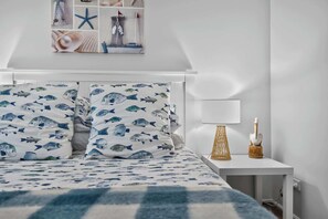 Un dormitorio con cama, almohadas, una mesita de noche con lámpara y un adorno en la pared.