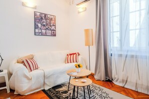 A cozy room with a white sofa, a small round table with a vase of flowers, a lamp, and a wall-mounted picture. - Cozy Studio in the Center of Zagreb (Zagreb)